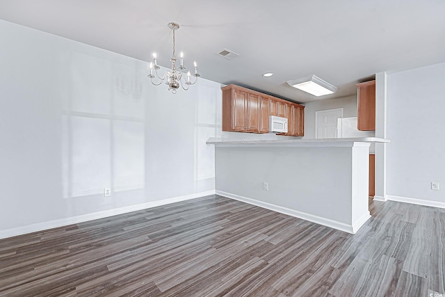 kitchen with a chandelier, white appliances, kitchen peninsula, and dark wood-type flooring