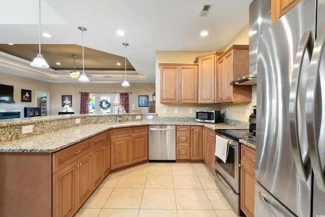 kitchen with light stone countertops, appliances with stainless steel finishes, a tray ceiling, sink, and decorative light fixtures