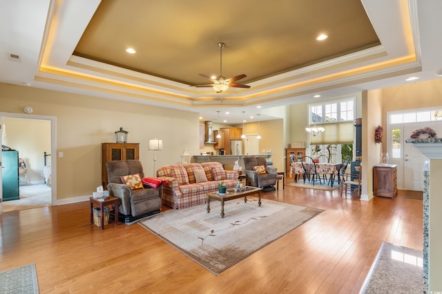 living room with ceiling fan with notable chandelier, a raised ceiling, and light hardwood / wood-style flooring