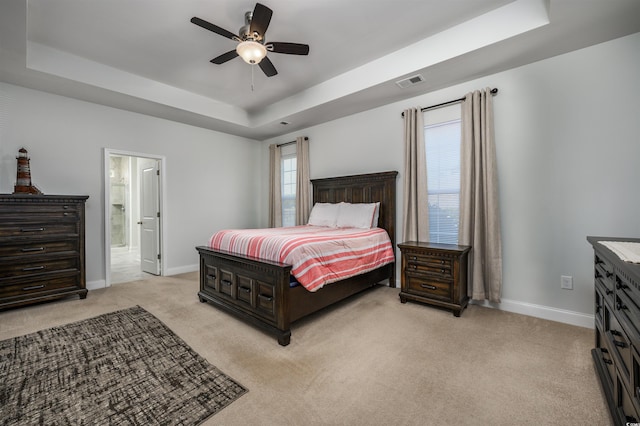 bedroom with ceiling fan, light carpet, connected bathroom, and a tray ceiling