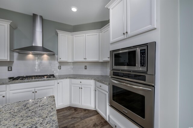 kitchen with white cabinetry, dark wood-type flooring, wall chimney range hood, and appliances with stainless steel finishes