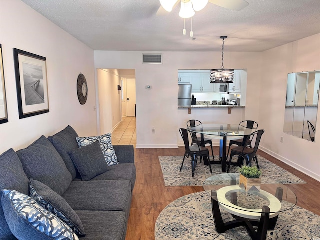 living room with ceiling fan with notable chandelier, light wood-type flooring, and a textured ceiling