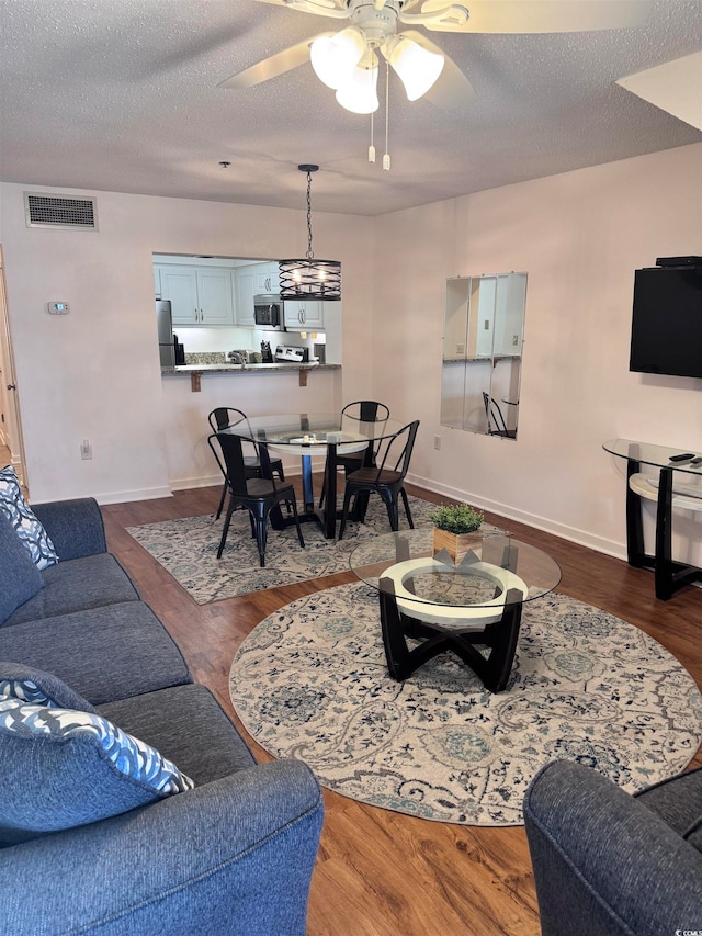 living room featuring hardwood / wood-style flooring, ceiling fan, and a textured ceiling