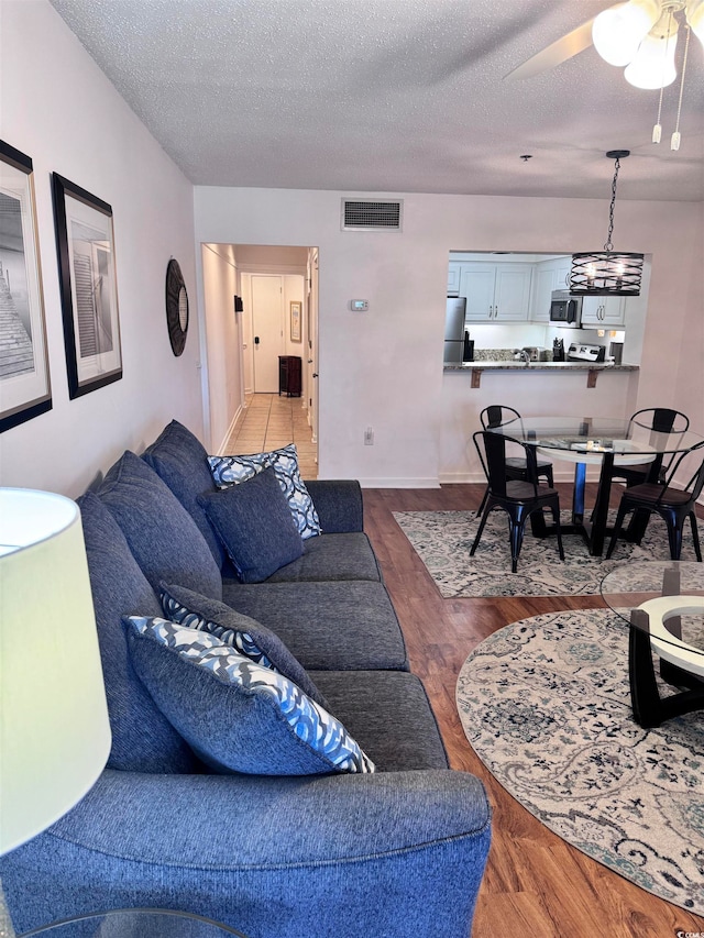 living room featuring ceiling fan with notable chandelier, wood-type flooring, and a textured ceiling