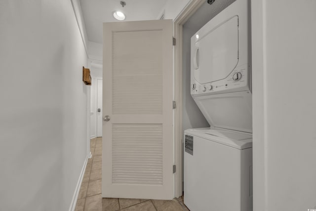 laundry area with stacked washer / drying machine and light tile patterned flooring