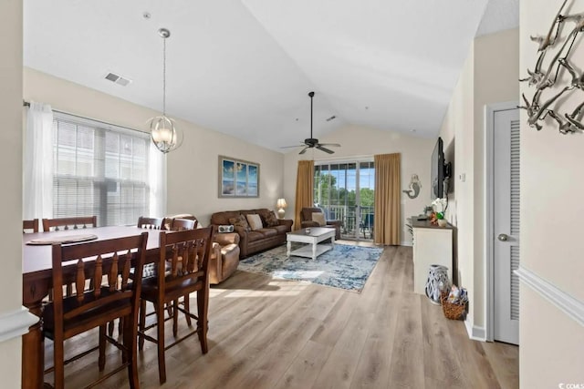 dining room with ceiling fan with notable chandelier, light hardwood / wood-style floors, and vaulted ceiling