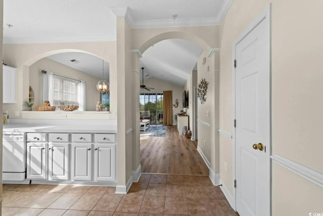 corridor featuring light tile patterned floors, ornamental molding, and vaulted ceiling