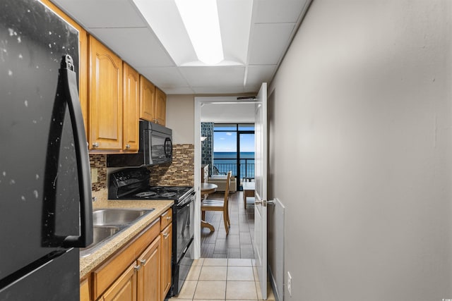 kitchen featuring tasteful backsplash, a drop ceiling, light tile patterned floors, and black appliances