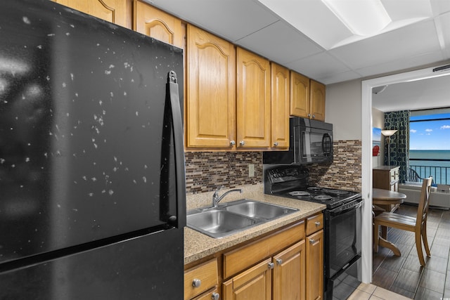 kitchen featuring sink, tasteful backsplash, a paneled ceiling, a water view, and black appliances