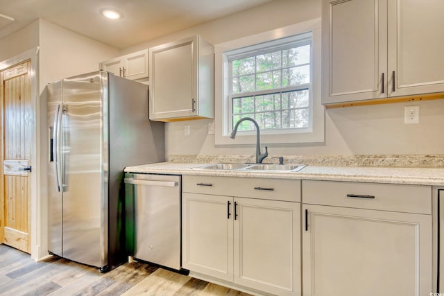 kitchen featuring light stone countertops, sink, stainless steel appliances, and light wood-type flooring