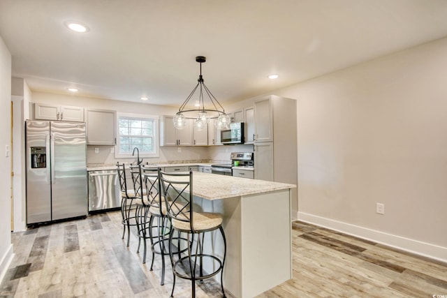 kitchen with light stone countertops, a center island, hanging light fixtures, appliances with stainless steel finishes, and light wood-type flooring