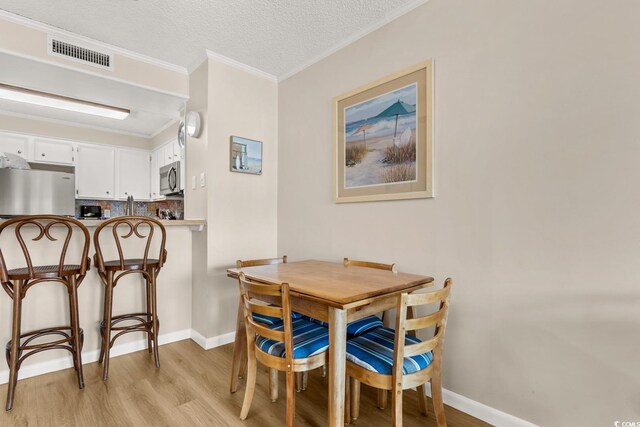 dining area with crown molding, light hardwood / wood-style floors, and a textured ceiling