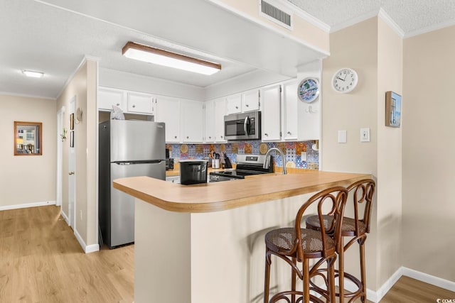 kitchen featuring kitchen peninsula, white cabinets, ornamental molding, and appliances with stainless steel finishes