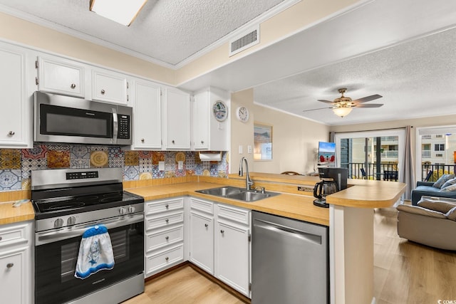 kitchen with sink, stainless steel appliances, kitchen peninsula, light hardwood / wood-style floors, and white cabinets