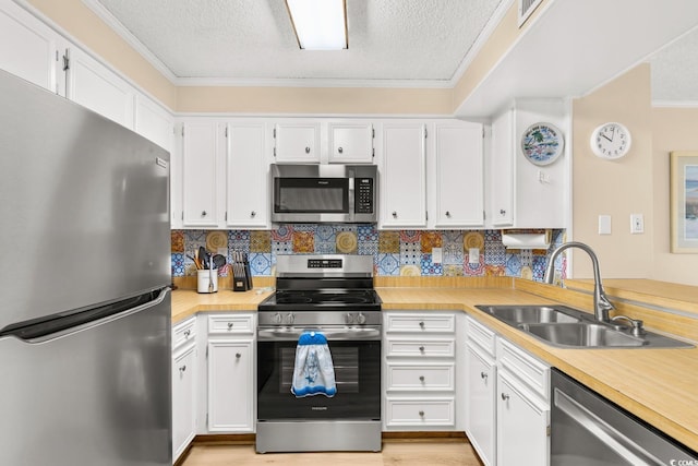 kitchen with backsplash, white cabinets, sink, ornamental molding, and stainless steel appliances