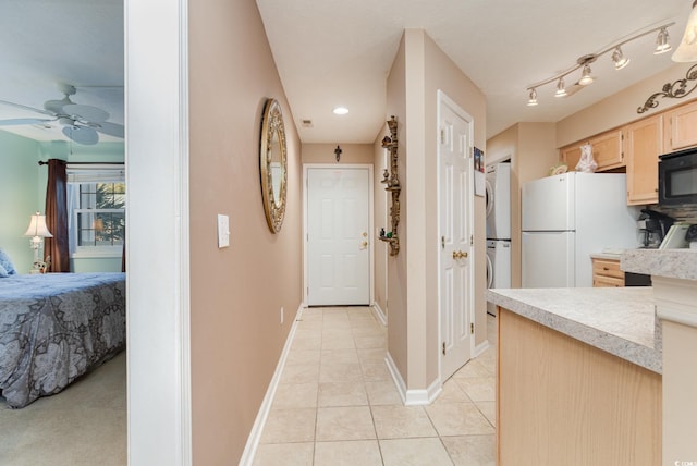 kitchen with light brown cabinetry, ceiling fan, white fridge, stacked washer / drying machine, and light tile patterned flooring