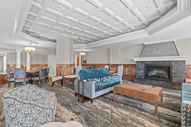 living room featuring decorative columns, a stone fireplace, coffered ceiling, and an inviting chandelier