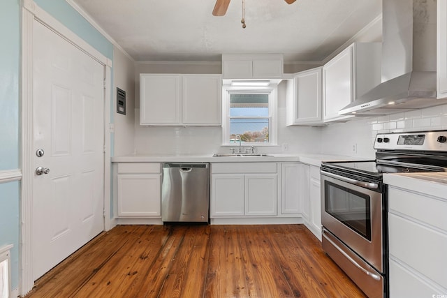 kitchen featuring ceiling fan, appliances with stainless steel finishes, wall chimney range hood, white cabinets, and sink