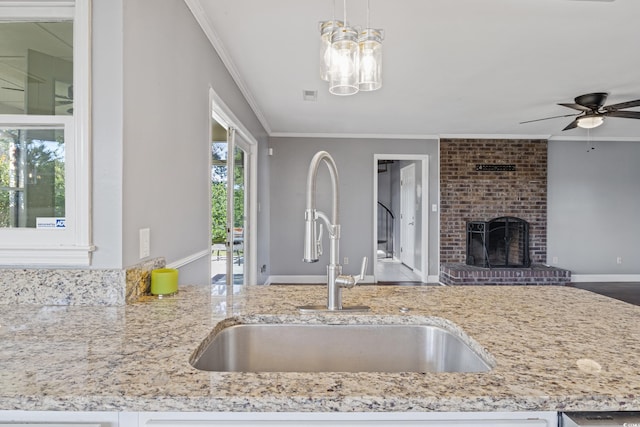 kitchen featuring ceiling fan, crown molding, sink, pendant lighting, and a fireplace