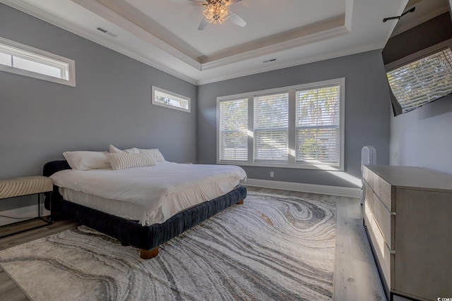 bedroom featuring a tray ceiling, light hardwood / wood-style flooring, ceiling fan, and ornamental molding