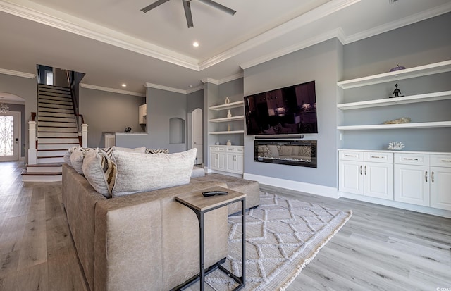 living room featuring ceiling fan, built in features, crown molding, and light hardwood / wood-style flooring