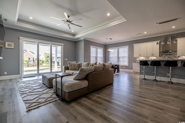 living room featuring dark hardwood / wood-style floors, crown molding, ceiling fan, and a tray ceiling