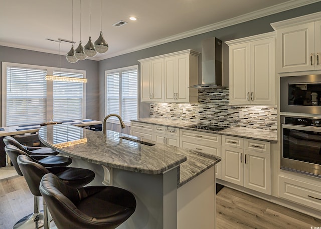 kitchen with light stone countertops, wall chimney exhaust hood, a healthy amount of sunlight, a center island with sink, and appliances with stainless steel finishes