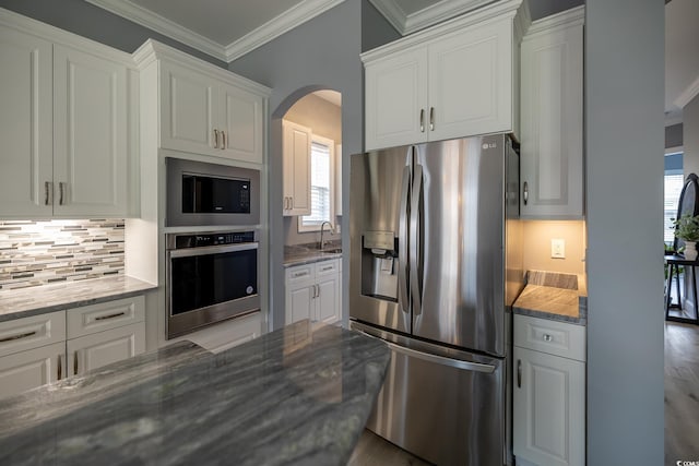 kitchen with appliances with stainless steel finishes, white cabinetry, a wealth of natural light, and dark stone counters