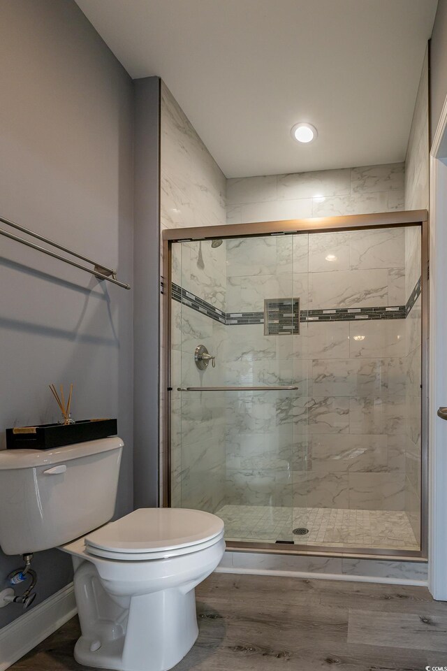 bathroom with wood-type flooring, toilet, and a shower with shower door