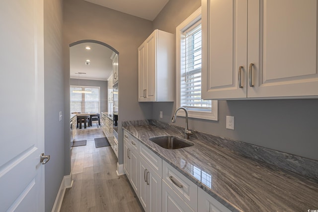 kitchen featuring light wood-type flooring, white cabinetry, dark stone counters, and sink