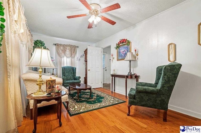 living area with wood-type flooring, a textured ceiling, ceiling fan, and crown molding