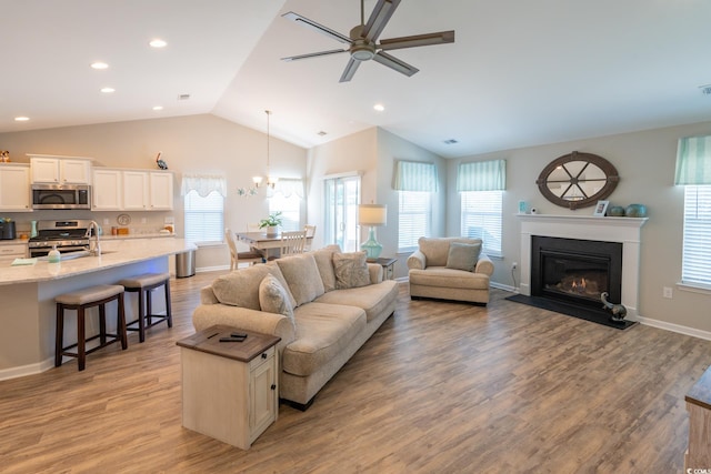 living room with ceiling fan with notable chandelier, light wood-type flooring, and vaulted ceiling