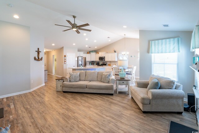 living room featuring ceiling fan with notable chandelier, light hardwood / wood-style floors, and lofted ceiling