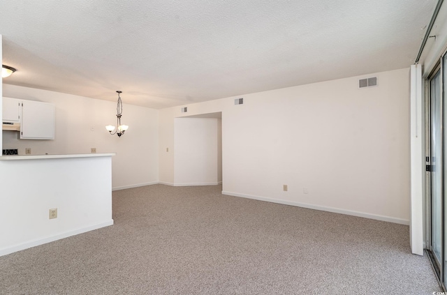 unfurnished living room with a textured ceiling, light colored carpet, and a notable chandelier