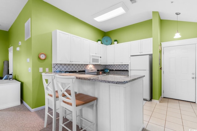 kitchen featuring backsplash, kitchen peninsula, white appliances, a breakfast bar area, and white cabinets