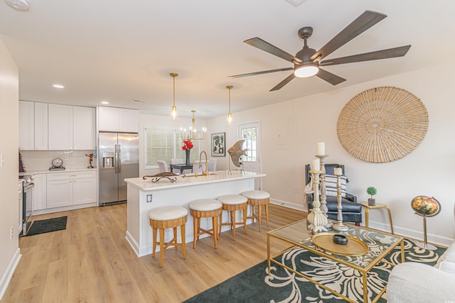 kitchen with an island with sink, decorative light fixtures, light hardwood / wood-style floors, white cabinetry, and stainless steel appliances