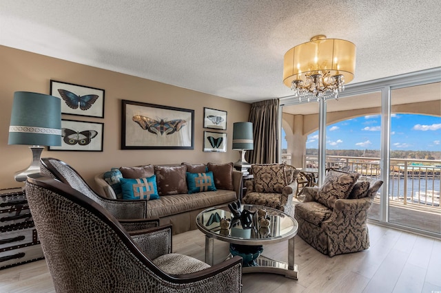 living room with a water view, a chandelier, a textured ceiling, and light wood-type flooring