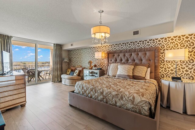 bedroom with access to outside, wood-type flooring, a notable chandelier, and a wall of windows