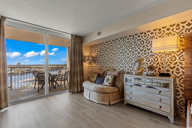 sitting room featuring wood-type flooring, a textured ceiling, a water view, and a wall of windows