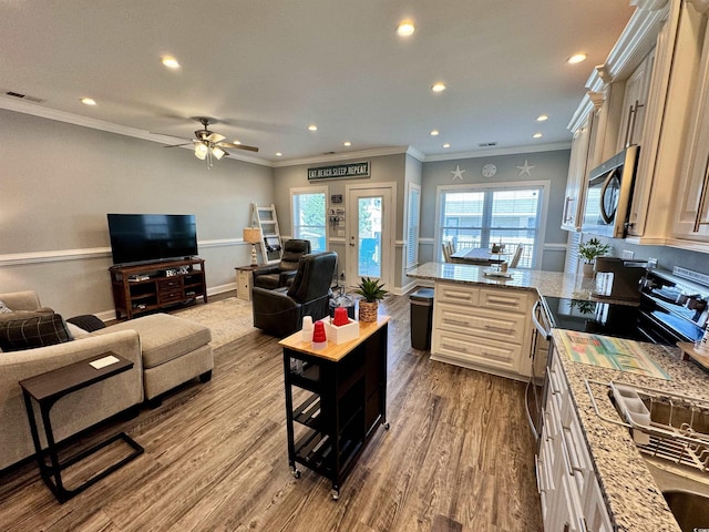 kitchen featuring ornamental molding, appliances with stainless steel finishes, cream cabinetry, light hardwood / wood-style floors, and light stone counters