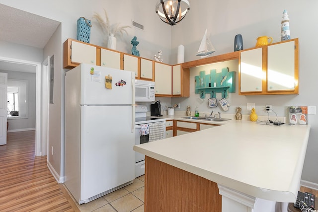 kitchen featuring white appliances, an inviting chandelier, sink, light hardwood / wood-style floors, and kitchen peninsula