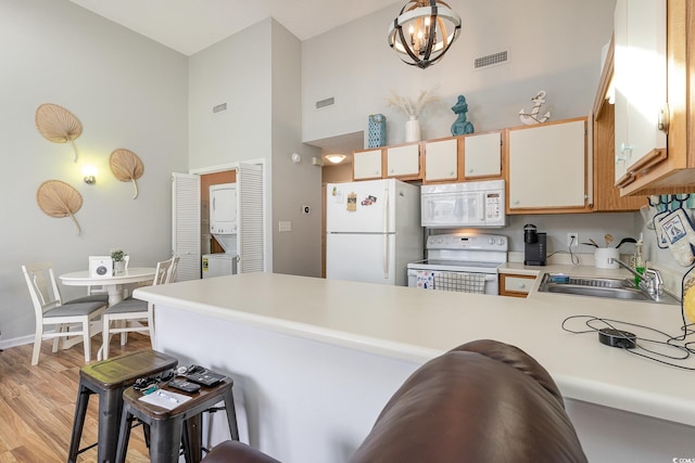 kitchen featuring pendant lighting, white appliances, sink, stacked washer / drying machine, and kitchen peninsula