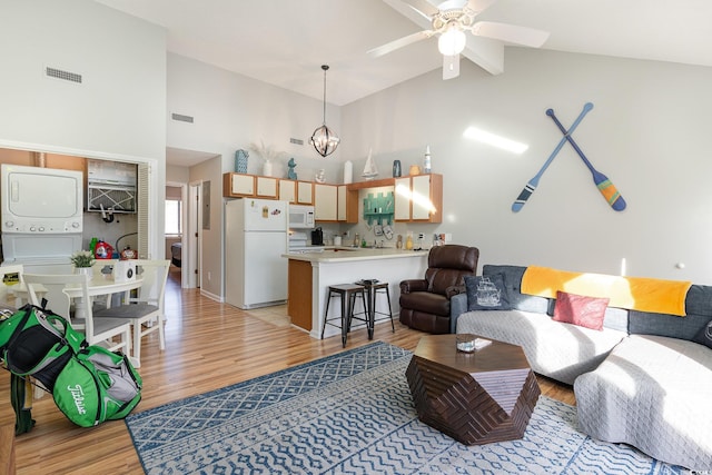 living room featuring ceiling fan with notable chandelier, light wood-type flooring, stacked washing maching and dryer, and high vaulted ceiling