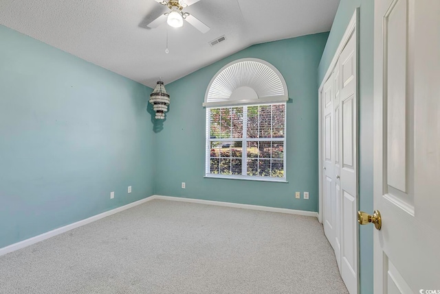 carpeted empty room with a textured ceiling, ceiling fan, and lofted ceiling