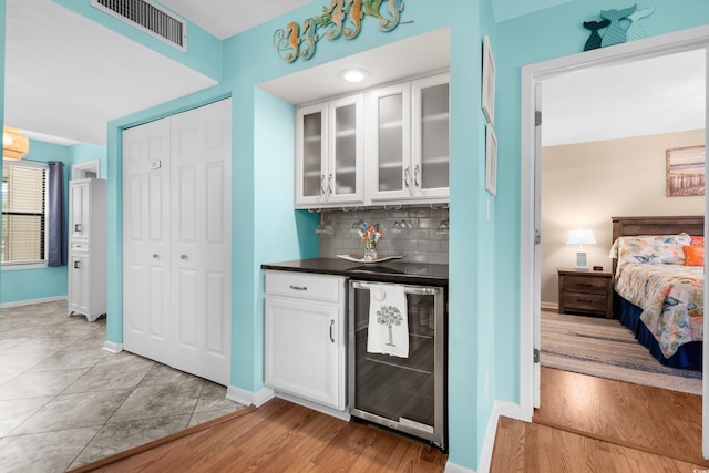 bar featuring light wood-type flooring, white cabinetry, beverage cooler, and backsplash