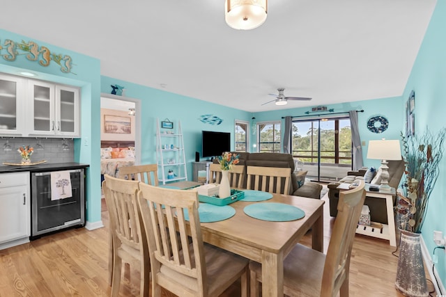 dining room featuring ceiling fan, beverage cooler, and light wood-type flooring