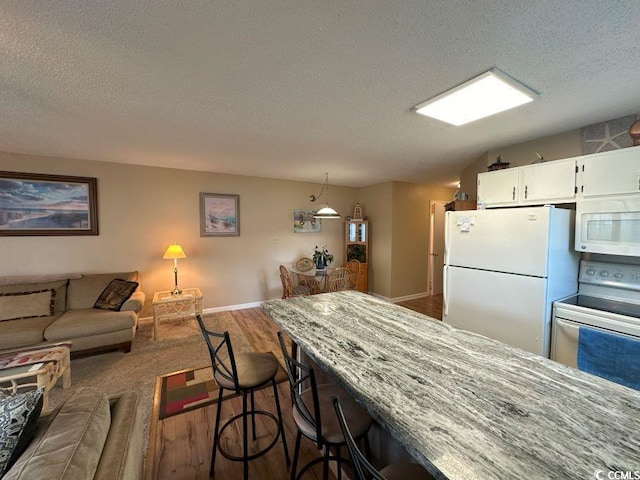 kitchen with a breakfast bar, white appliances, a textured ceiling, hardwood / wood-style floors, and white cabinetry