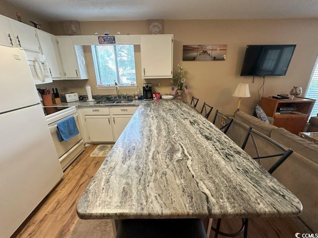 kitchen featuring a breakfast bar, white appliances, sink, and light hardwood / wood-style flooring