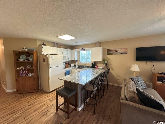 kitchen with white cabinets, light wood-type flooring, white appliances, and a textured ceiling