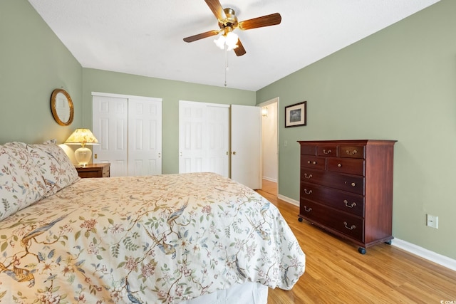 bedroom featuring ceiling fan, two closets, and light hardwood / wood-style flooring